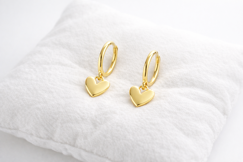 Gold heart-shaped earrings on a white cushion