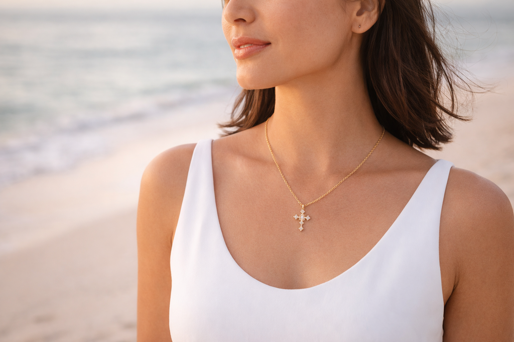 Woman wearing a white tank top and gold necklace with a cross pendant on a beach.