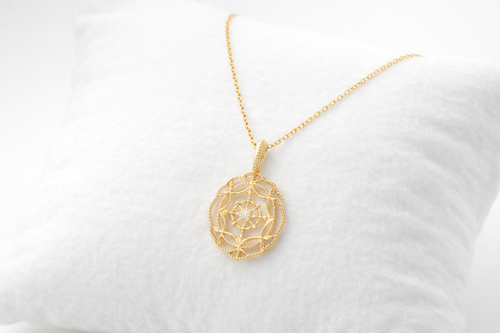 Gold necklace with a intricate pendant on a white cushion