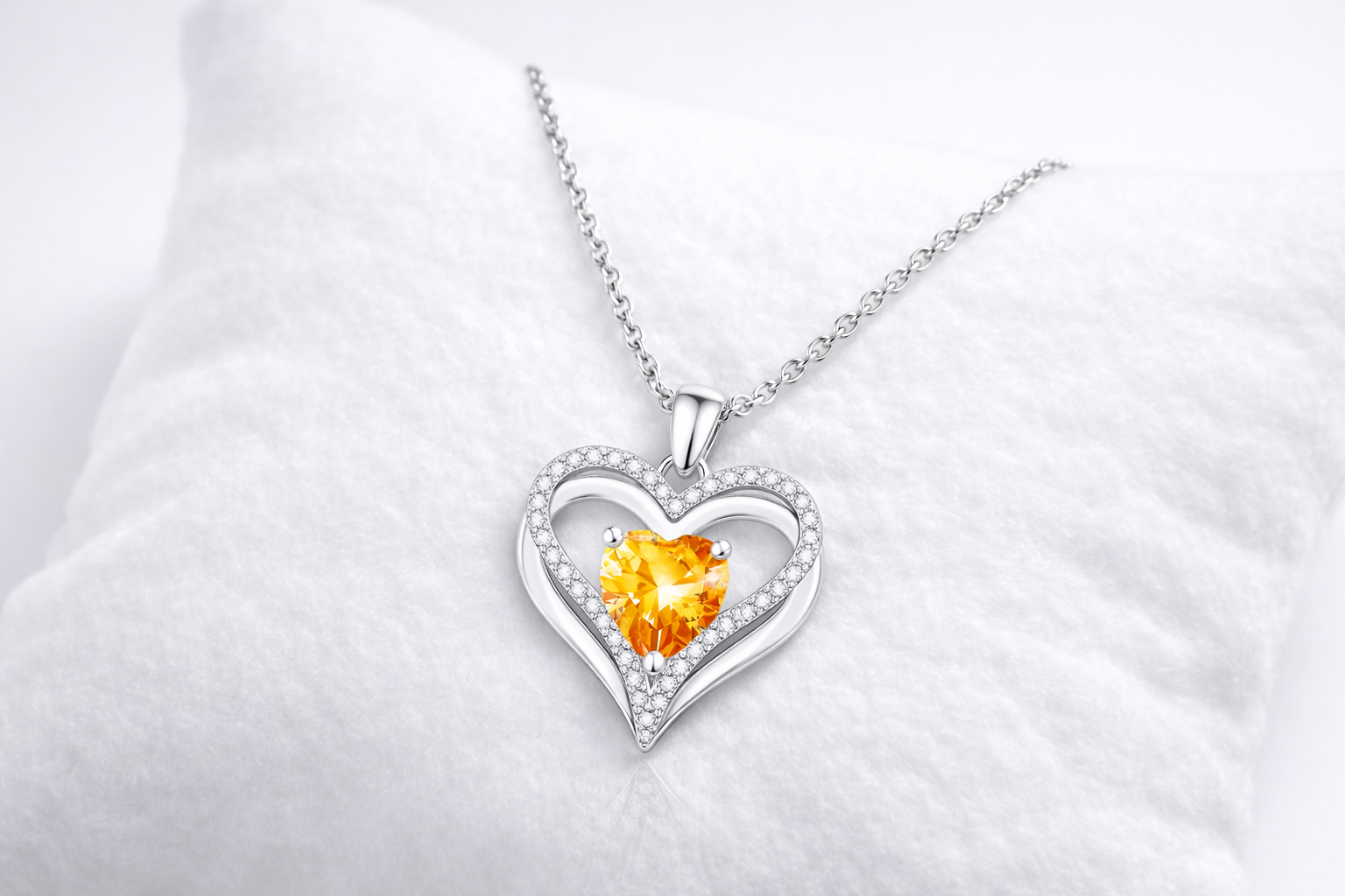 Heart-shaped silver pendant with a yellow gemstone on a white background