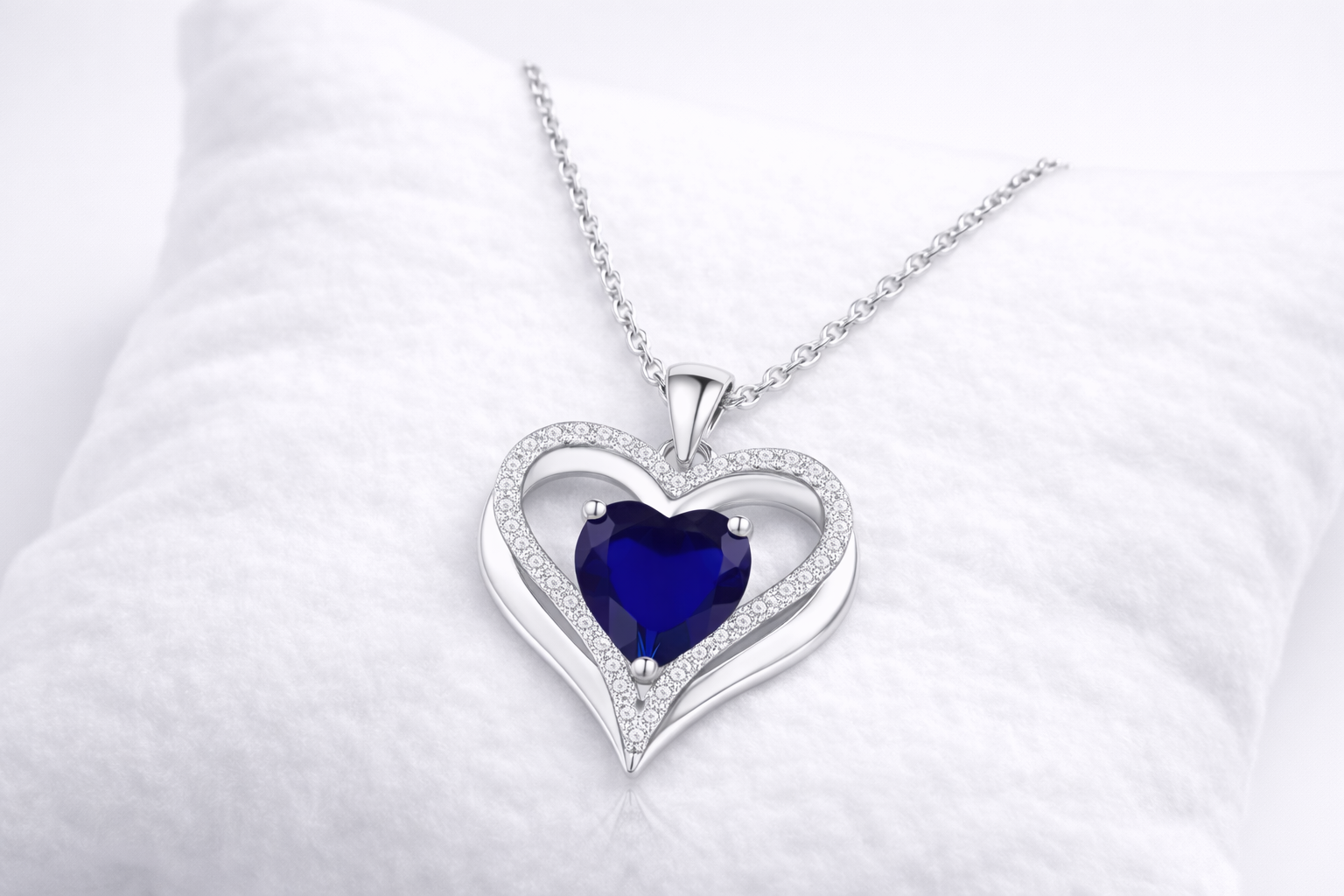Heart-shaped silver pendant with a blue gemstone on a white background