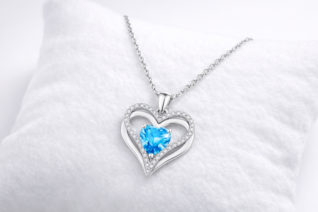 Heart-shaped silver necklace with a blue gemstone on a white background