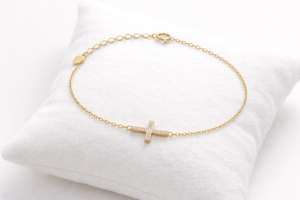 Gold bracelet with a small cross pendant on a white cushion