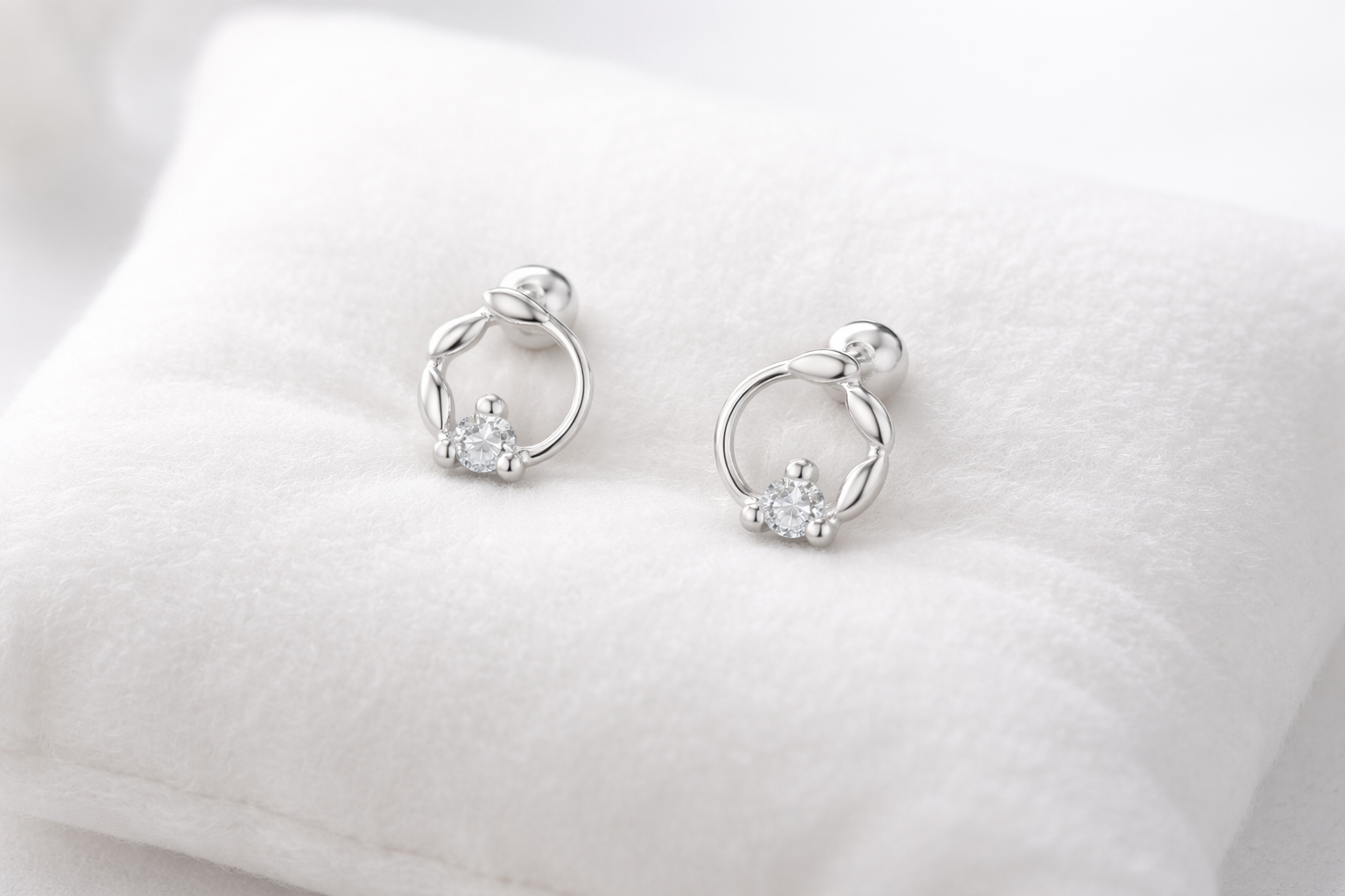 Pair of silver earrings with small diamonds on a white cushion