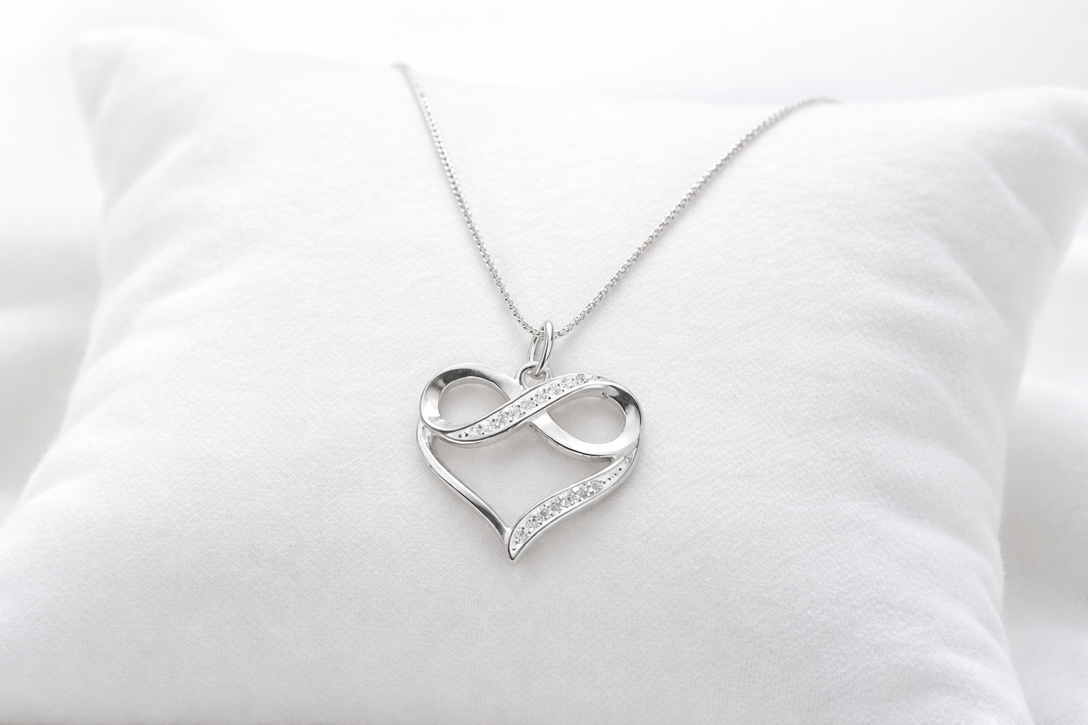 Silver heart-shaped pendant with infinity symbol on a white cushion