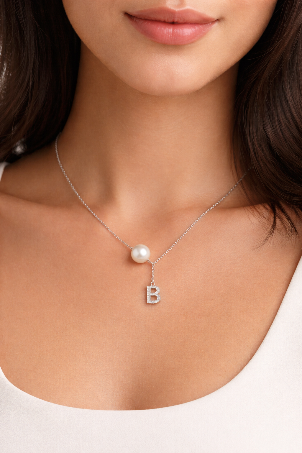 Necklace with a pearl and letter 'B' pendant on a person wearing a white top.