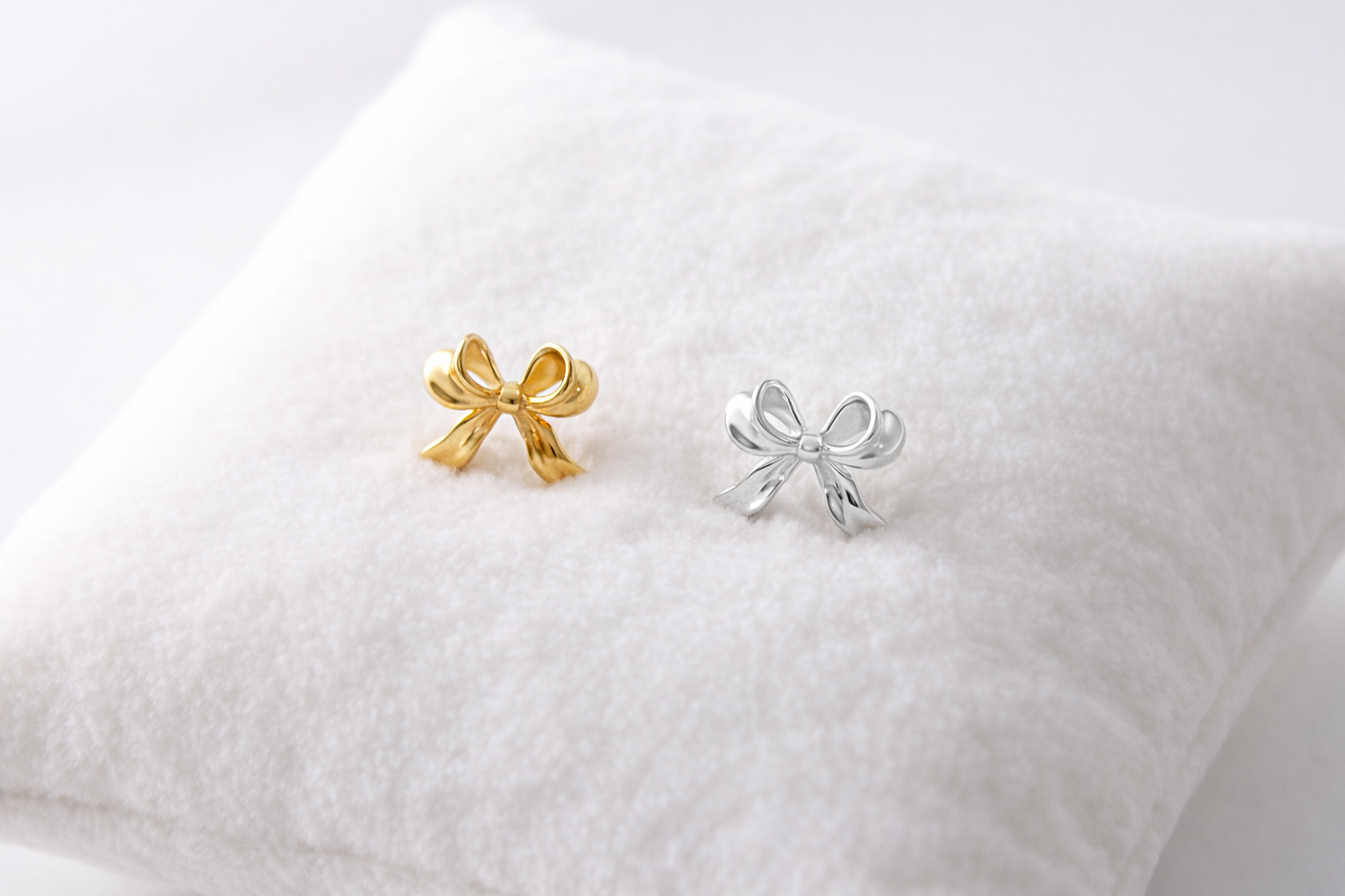 Gold and silver bow-shaped earrings on a white pillow