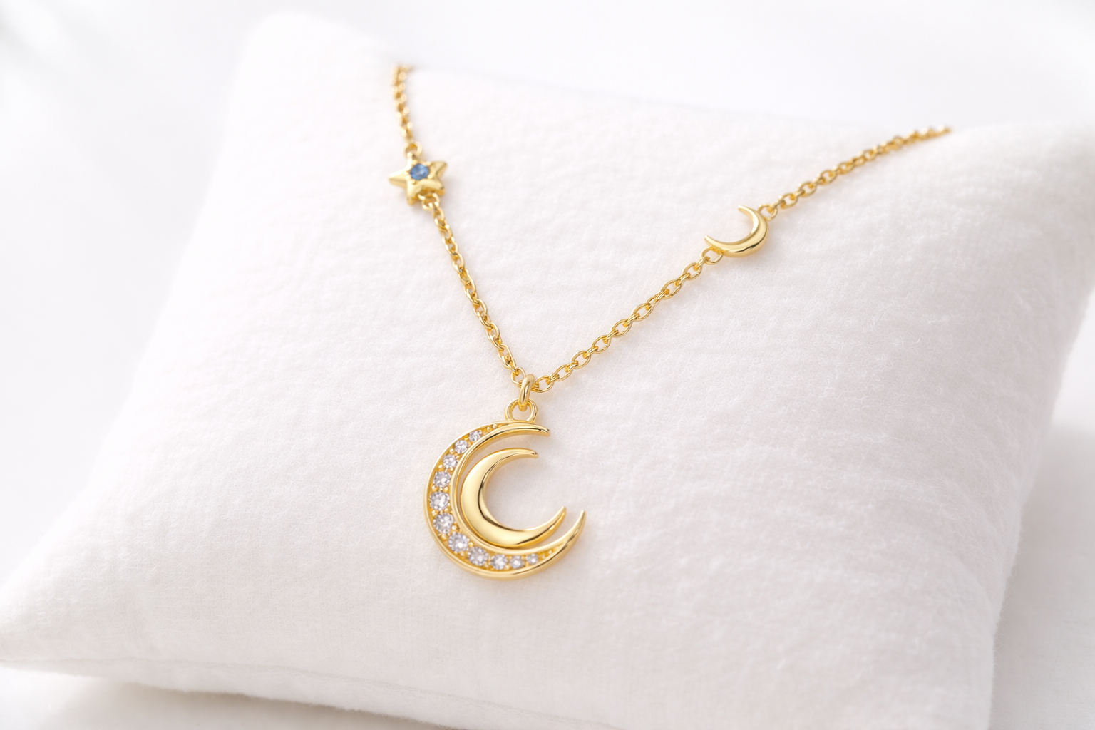 Gold necklace with a crescent moon pendant on a white cushion