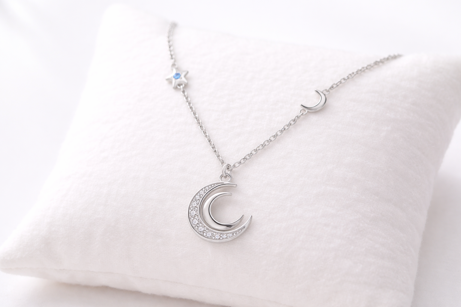 Silver necklace with a crescent moon pendant on a white cushion