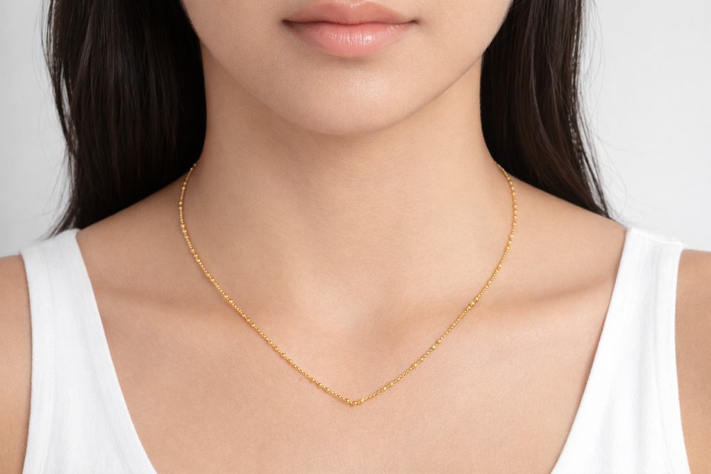 Gold necklace worn by a person against a neutral background