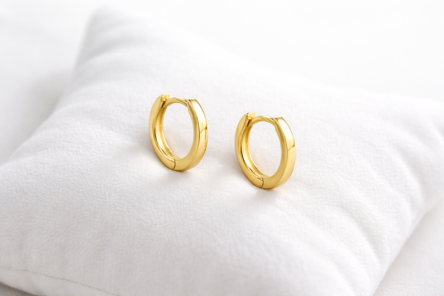 Gold hoop earrings on a white fabric background