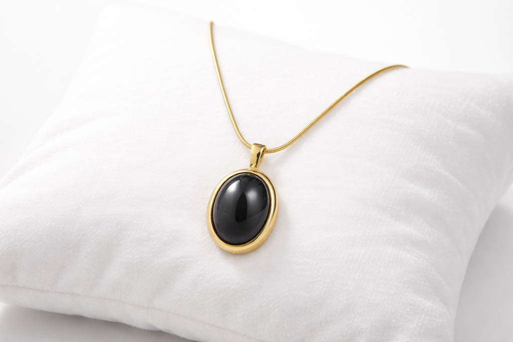 Gold necklace with a black pendant on a white cushion