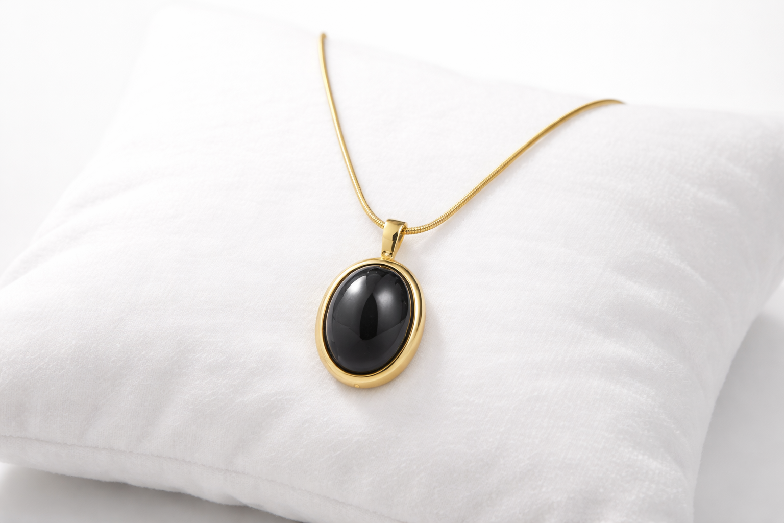 Gold necklace with a black pendant on a white cushion
