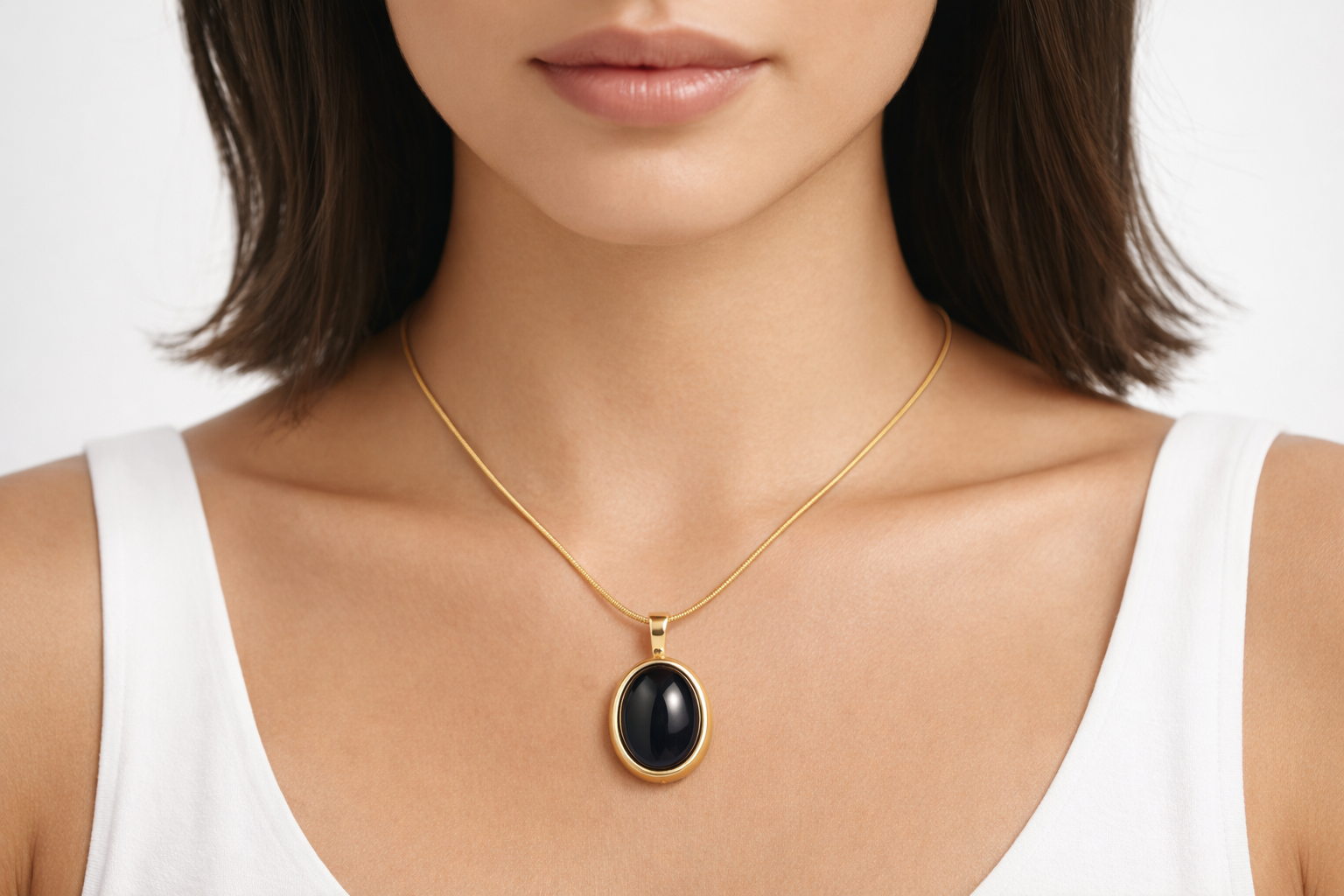 Woman wearing a gold necklace with a black pendant on a white background