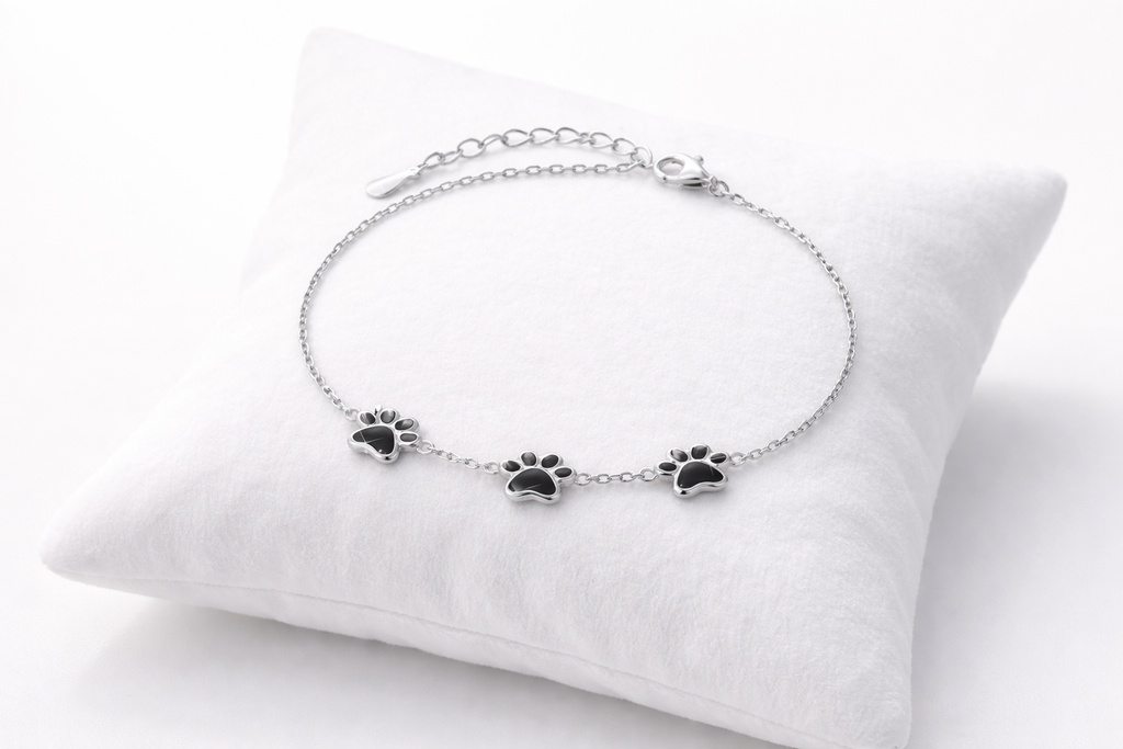 Silver bracelet with paw print charms on a white cushion