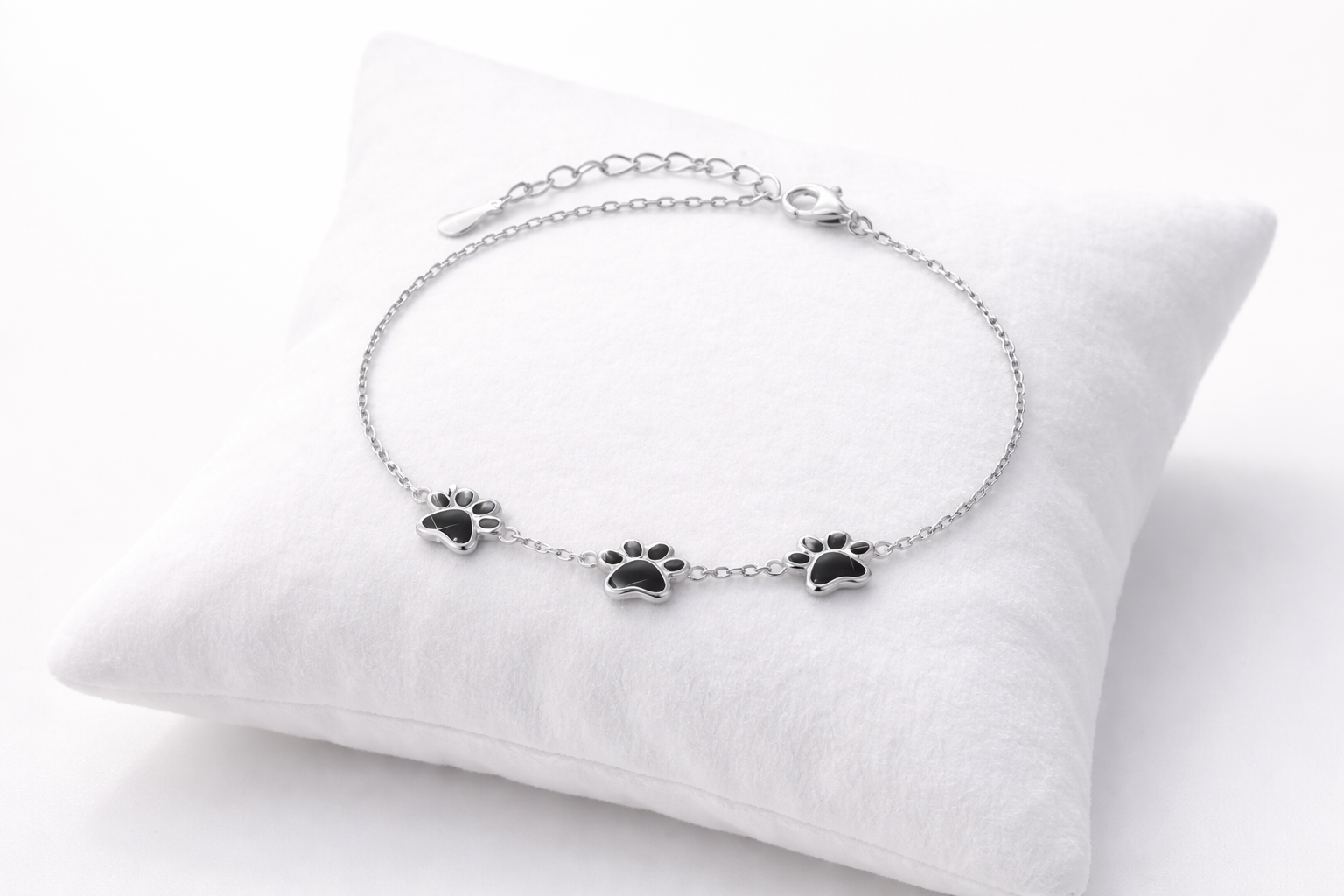 Silver bracelet with paw print charms on a white cushion