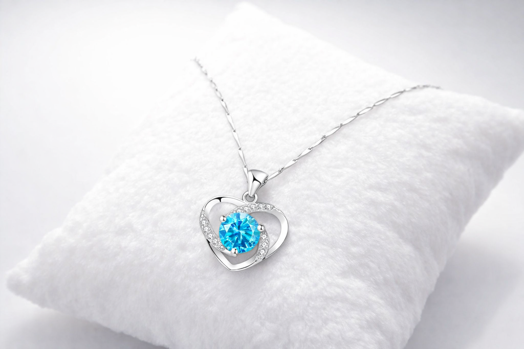 Heart-shaped silver pendant with a blue gemstone on a white cushion