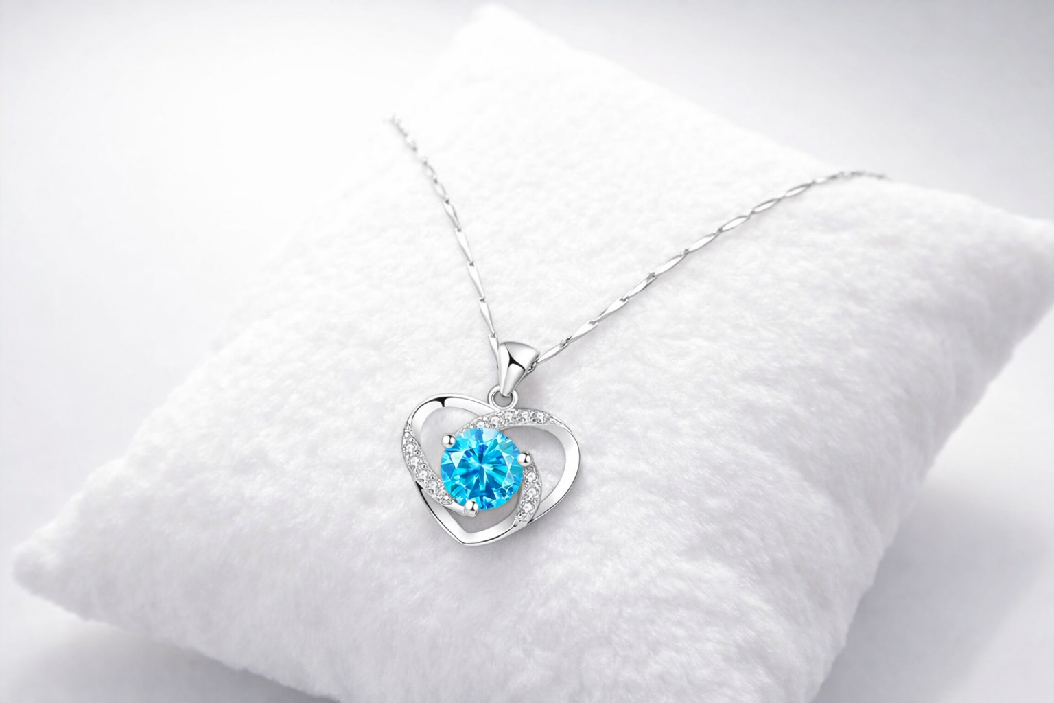 Heart-shaped silver pendant with a blue gemstone on a white cushion