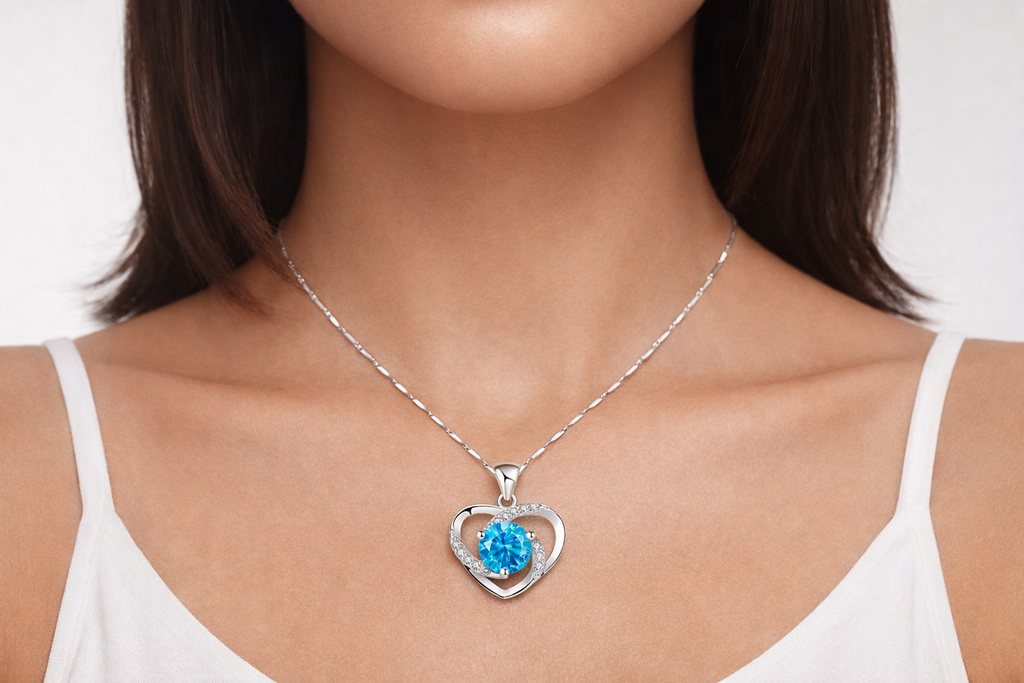 Necklace with a heart-shaped pendant featuring a blue gemstone on a model wearing a white top.
