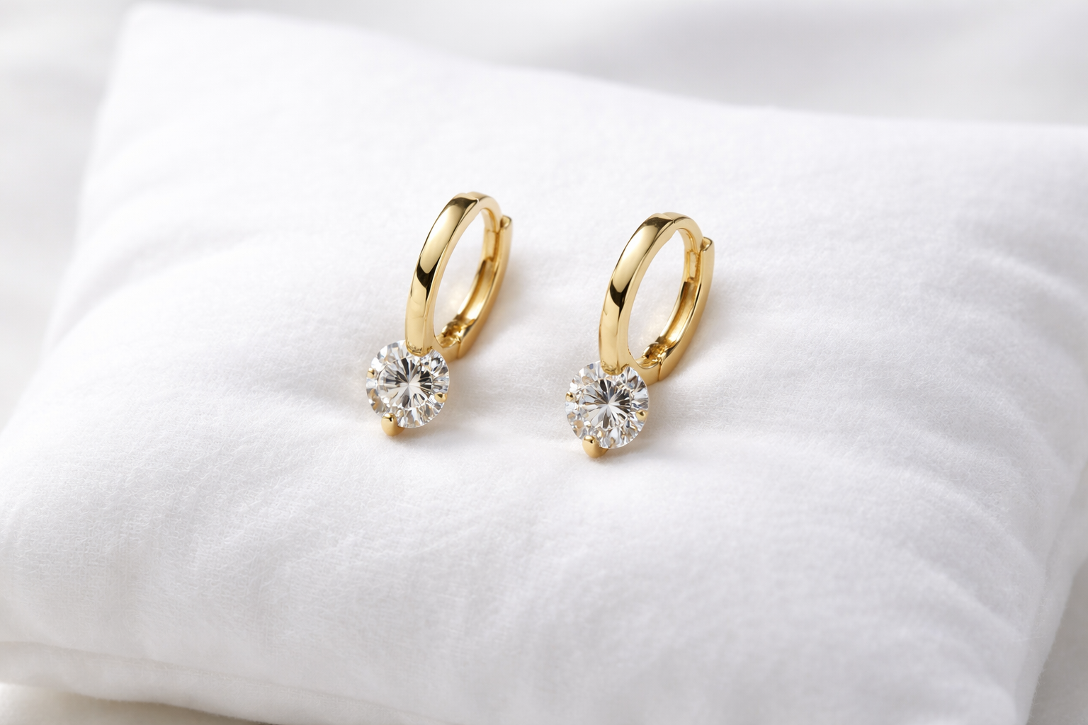 Gold hoop earrings with clear gemstones on a white cushion