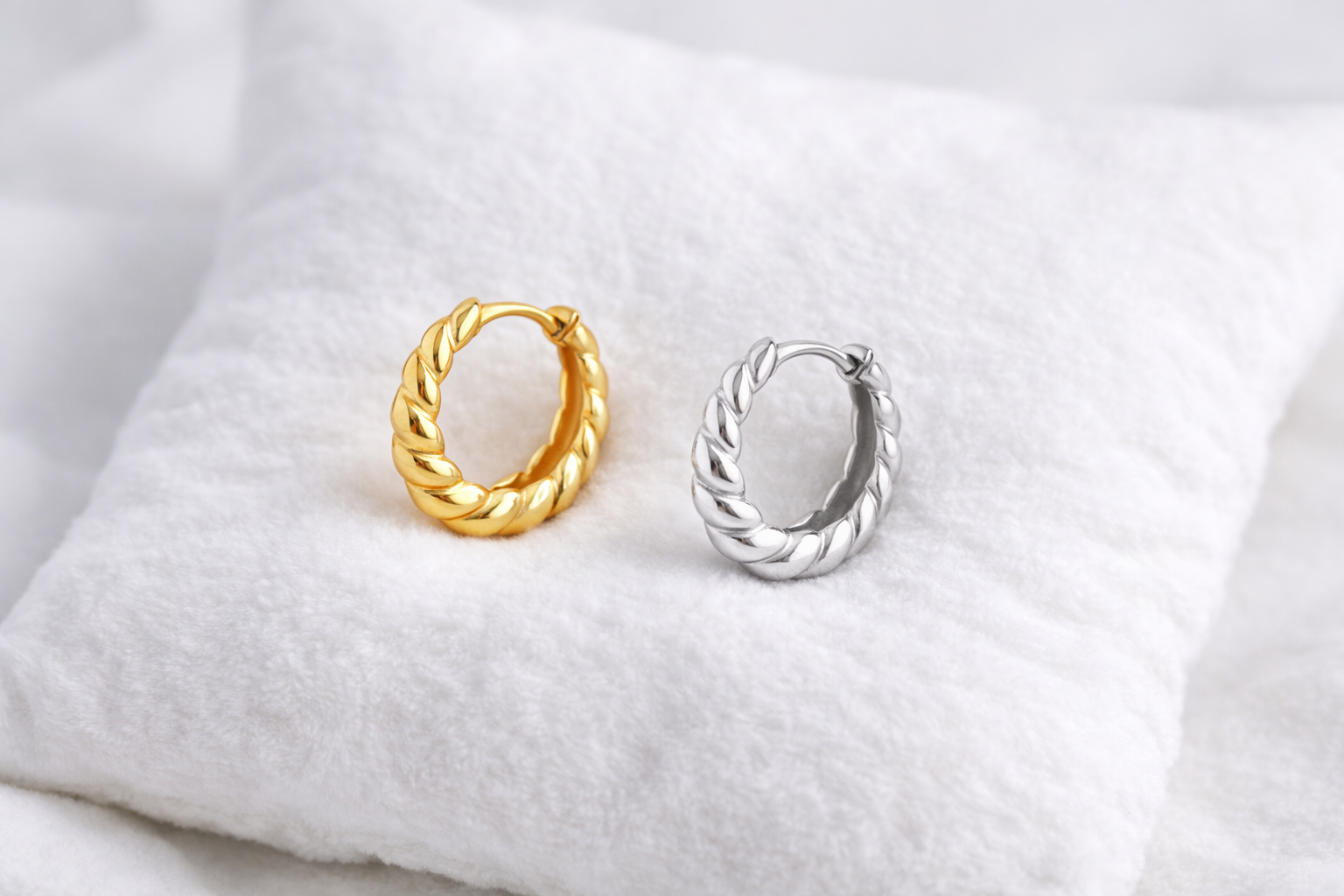 Gold and silver hoop earrings on a white fabric background