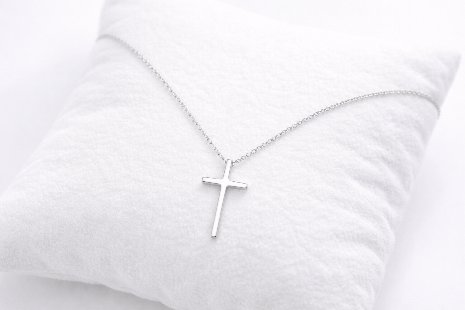 Silver cross necklace on a white pillow
