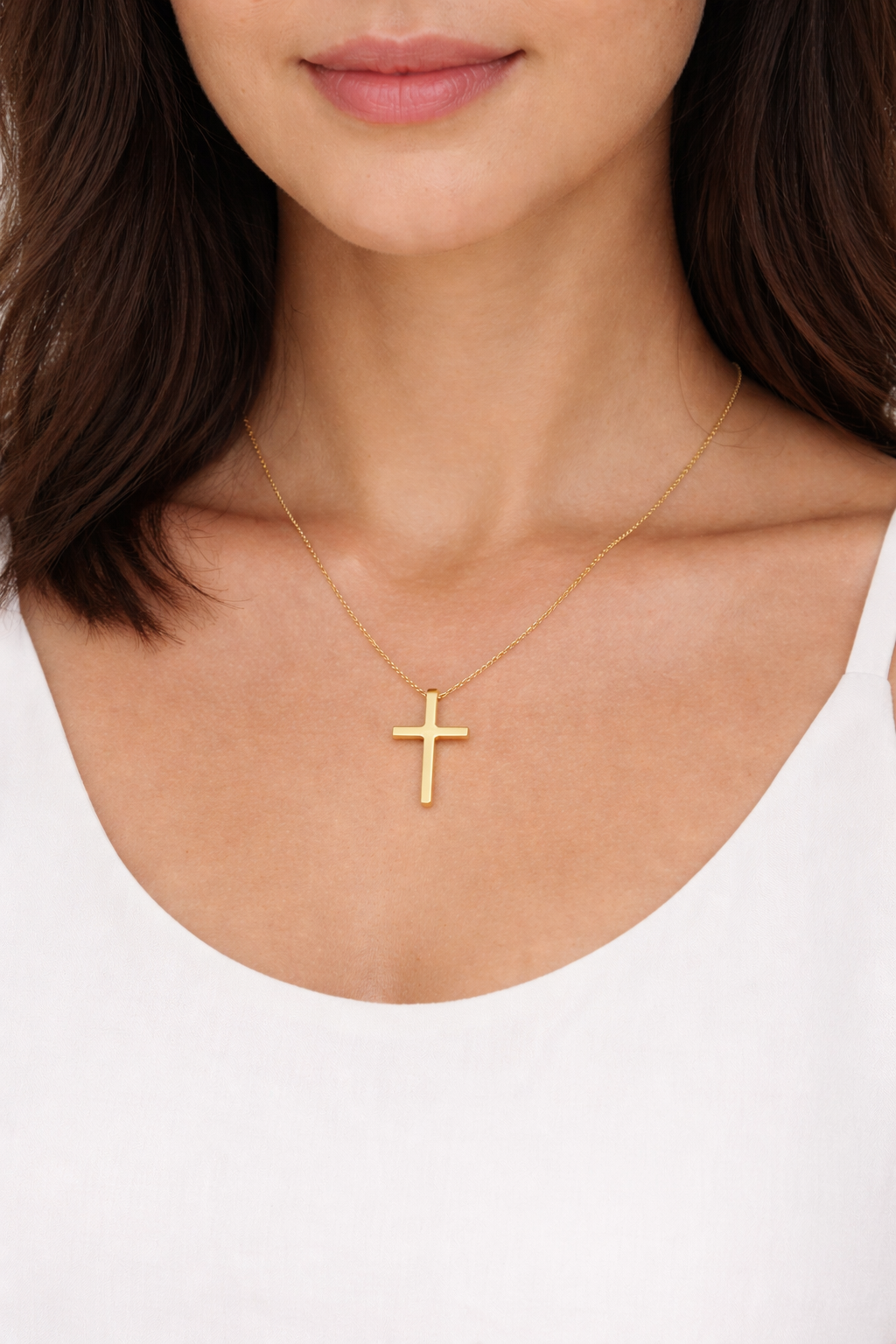 Gold cross necklace on a person wearing a white top