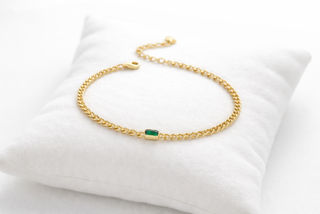 Gold bracelet with a green gemstone on a white cushion
