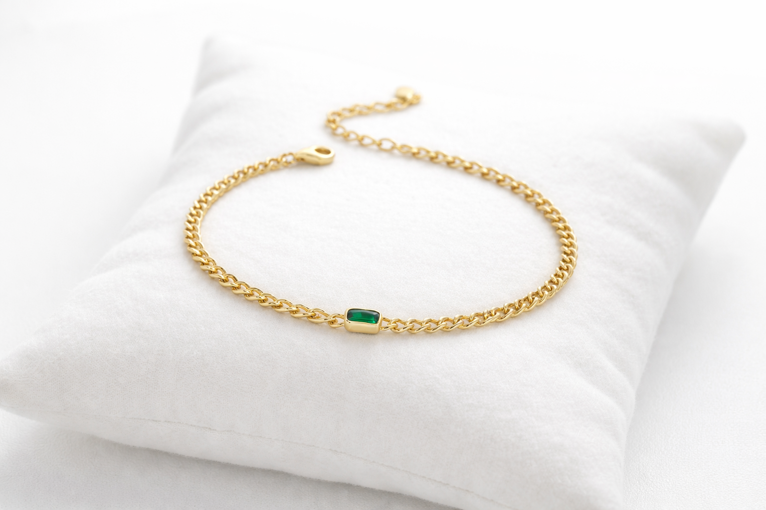 Gold bracelet with a green gemstone on a white cushion