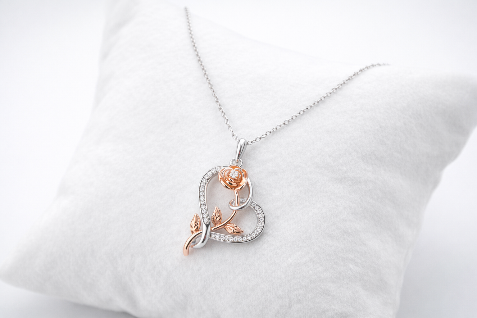 Rose gold and silver necklace with a heart-shaped pendant on a white cushion